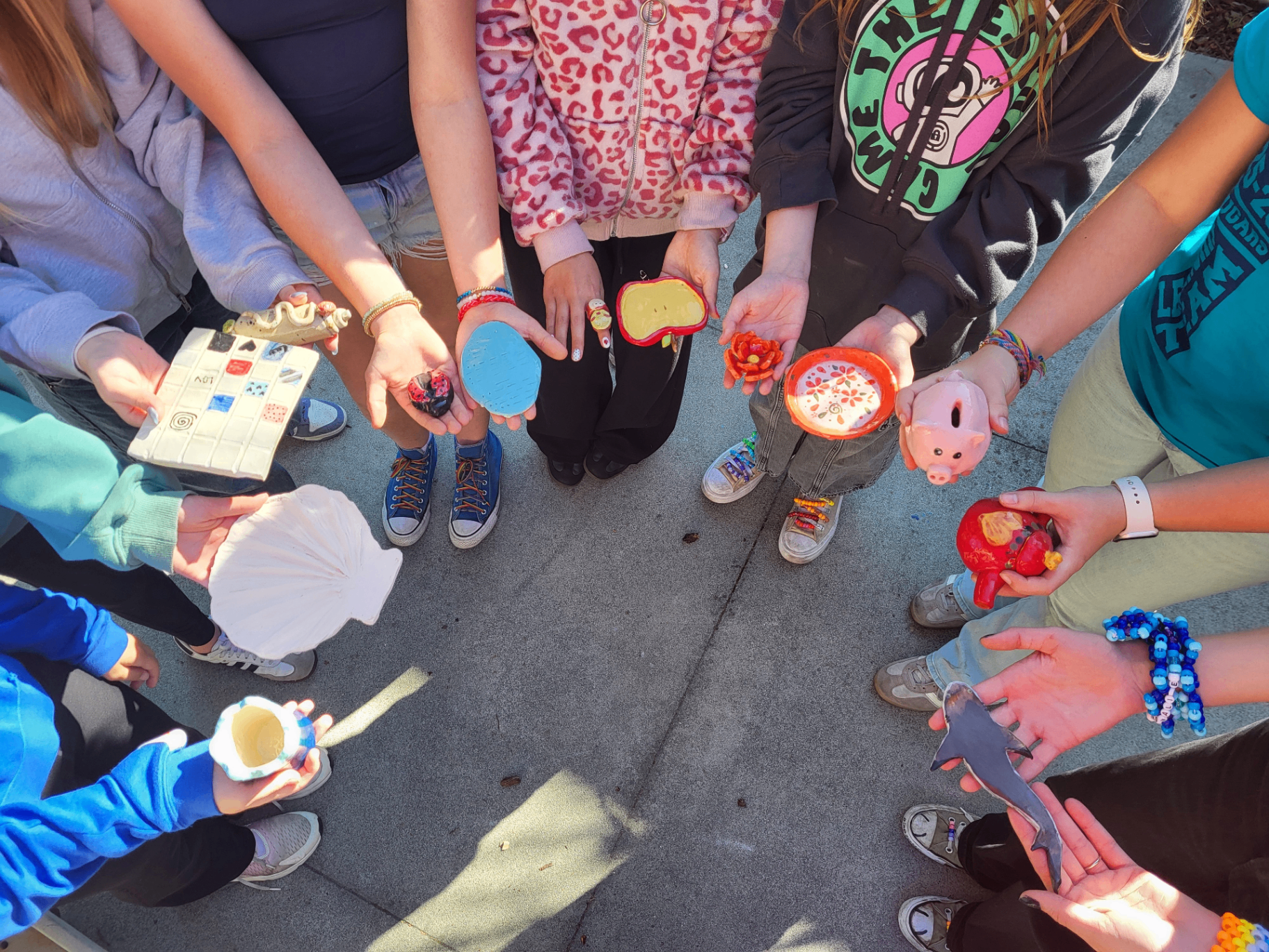 Students proudly showing their handmade pottery and clay creations in a circle
